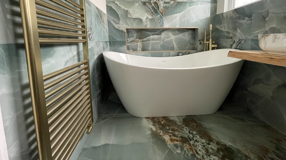 Freestanding bath surrounded by green stone-effect wall and floor tiles